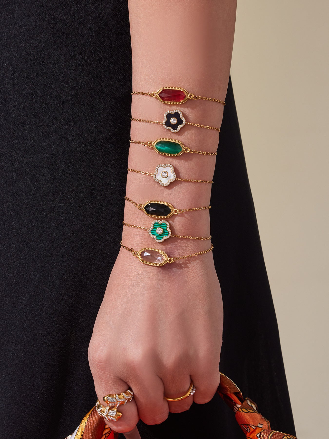 Hand wearing multiple gold bracelets with gemstone accents on a neutral background