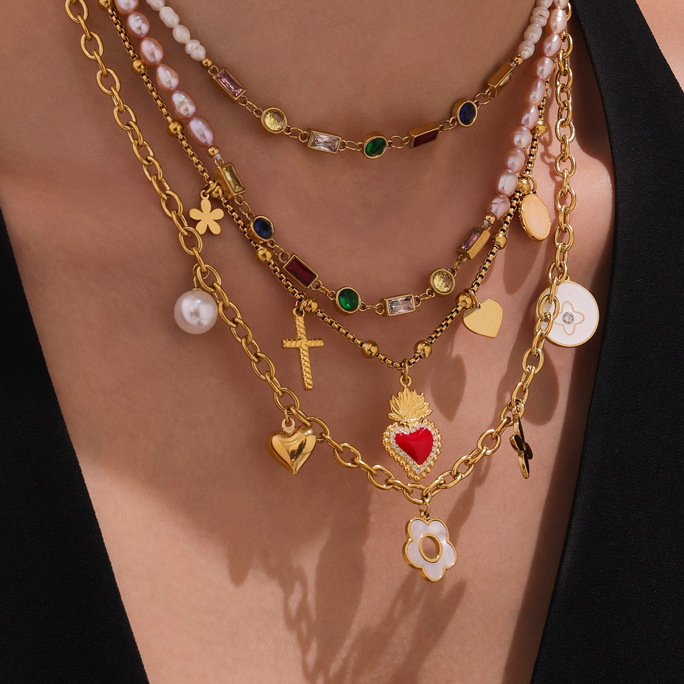 Multiple gold necklaces with various charms on a person wearing a black top.