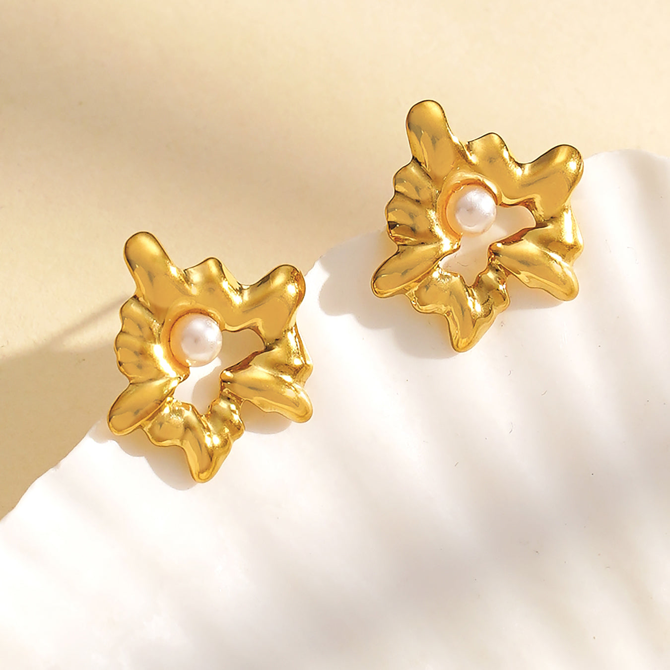 Gold earrings with pearl centers on a beige background